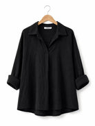 A black long-sleeve shirt with a relaxed, oversized fit, displayed on a wooden hanger against a plain white background.