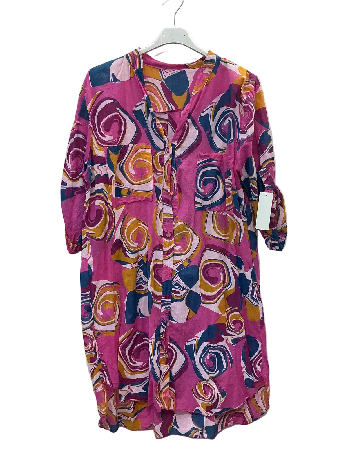 A pink long-sleeve tunic dress with a bold abstract swirl pattern in yellow, orange, navy, and white, hanging on a white hanger against a plain white wall.