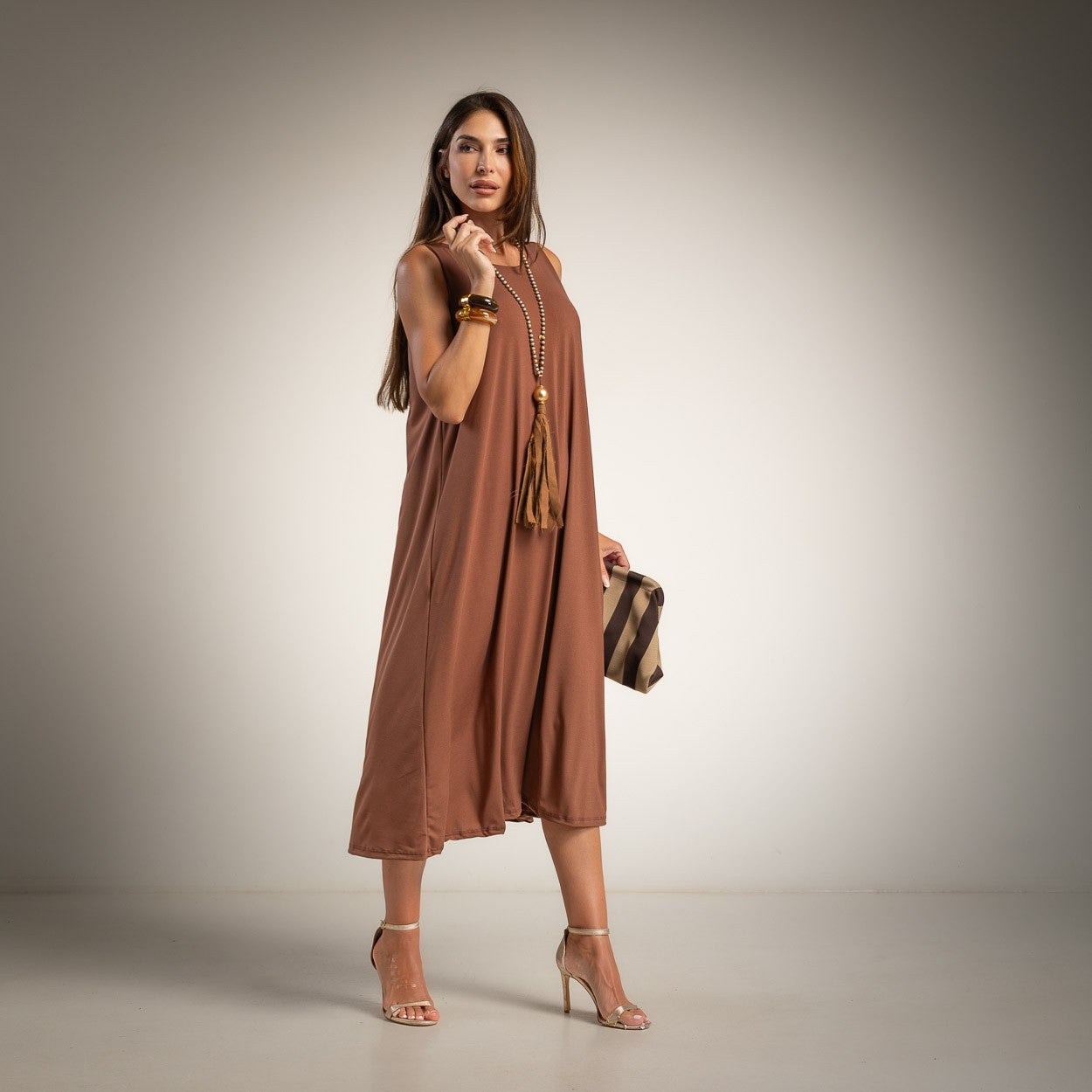 A woman models a sleeveless, flowy midi dress in a warm brown shade. 