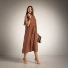 A woman models a sleeveless, flowy midi dress in a warm brown shade. 