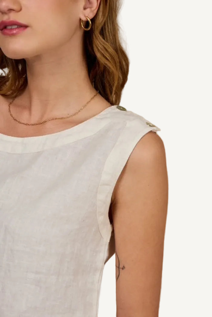 Close-up of a person wearing a light-colored sleeveless top against a beige background