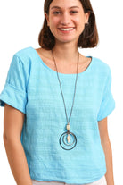 Woman wearing a blue top and a long necklace with a beige background