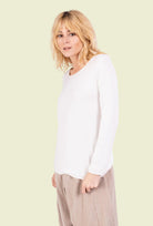 Woman wearing a white long-sleeve top and beige pants on a white background