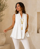 A woman wearing a sleeveless white wrap-style top and white pants