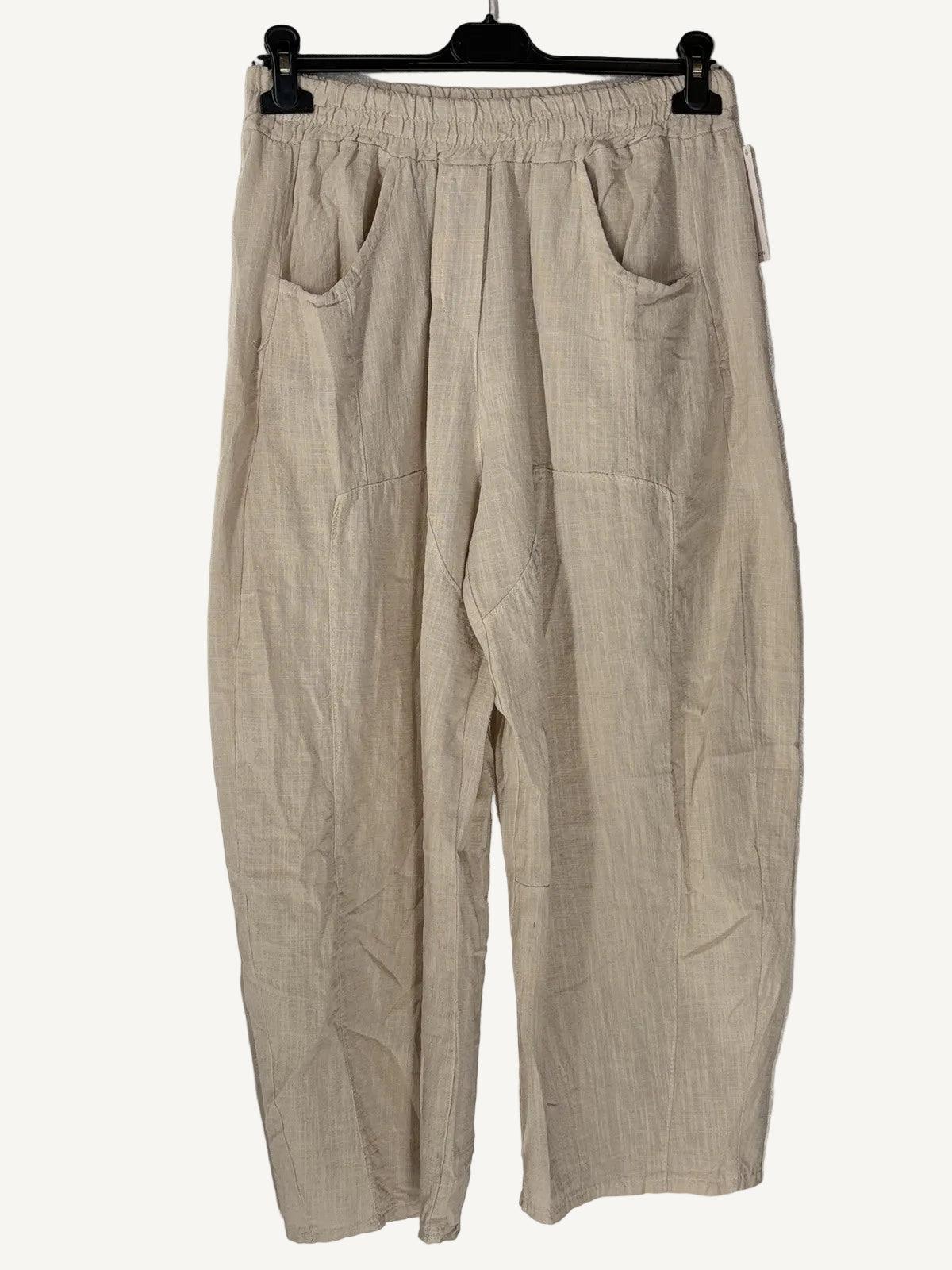 Beige pants hanging on a hanger against a textured white wall