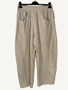 Beige pants hanging on a hanger against a textured white wall