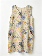 A sleeveless cream-colored dress with a blue, pink, and yellow floral pattern, featuring side pockets, shown against a plain white background.