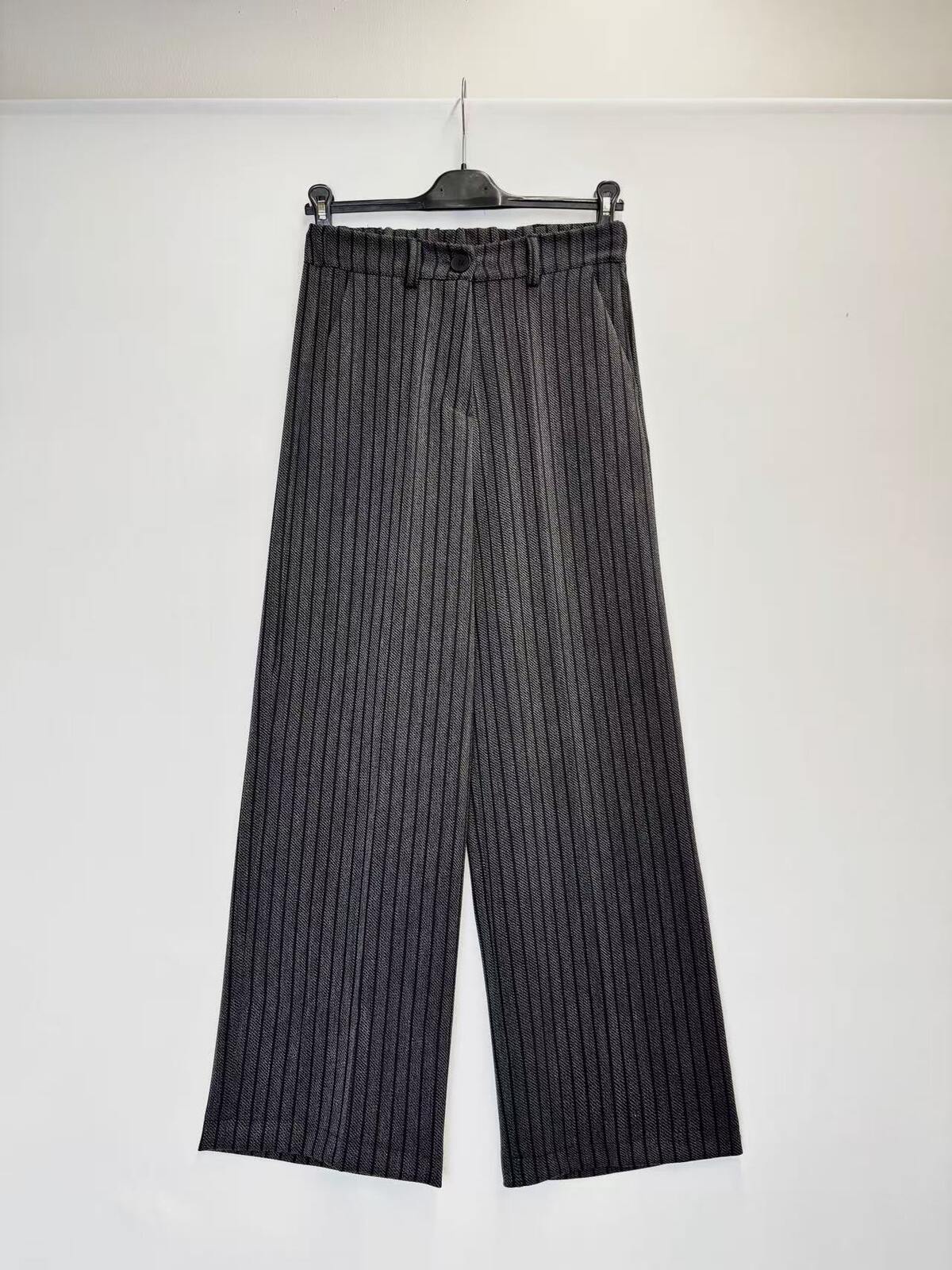 A pair of wide-leg cropped trousers with vertical pinstripes, hanging on a black hanger against a plain white wall.