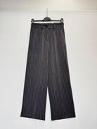 A pair of wide-leg cropped trousers with vertical pinstripes, hanging on a black hanger against a plain white wall.