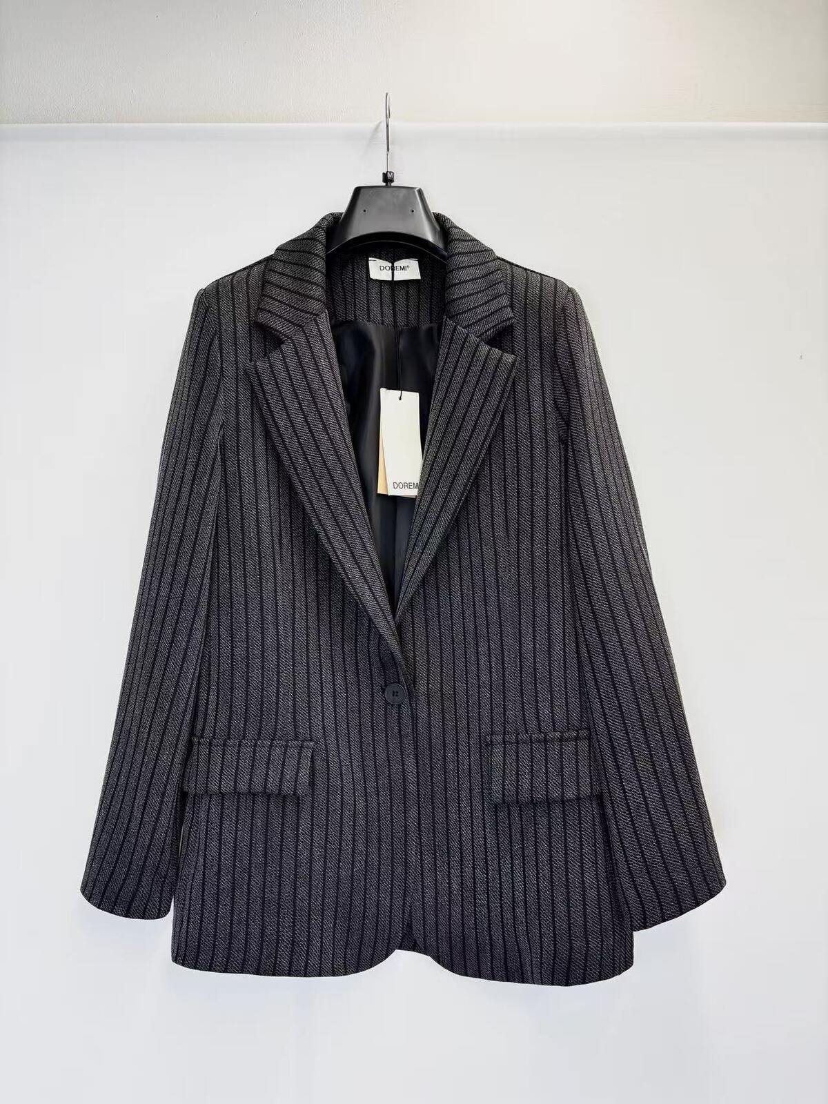 A dark gray pinstripe blazer jacket hanging on a black hanger against a plain white wall, with a white price tag still attached.