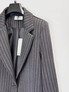 A close-up of a grey pinstripe blazer hanging on a black hanger against a plain white background. 