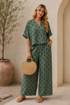 Woman in a green polka dot outfit holding a woven bag indoors.