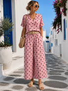 Woman in a pink polka dot dress standing on a picturesque street with white buildings and blue doors.