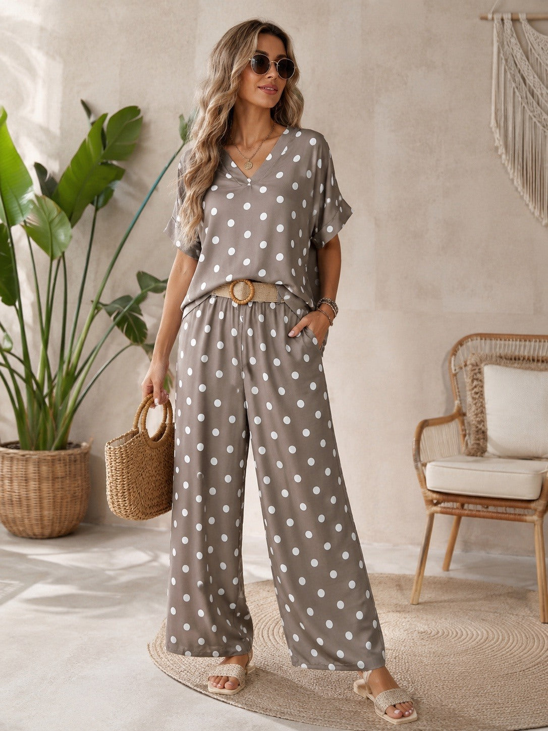 Woman in a polka dot outfit standing in a room with plants and a chair.