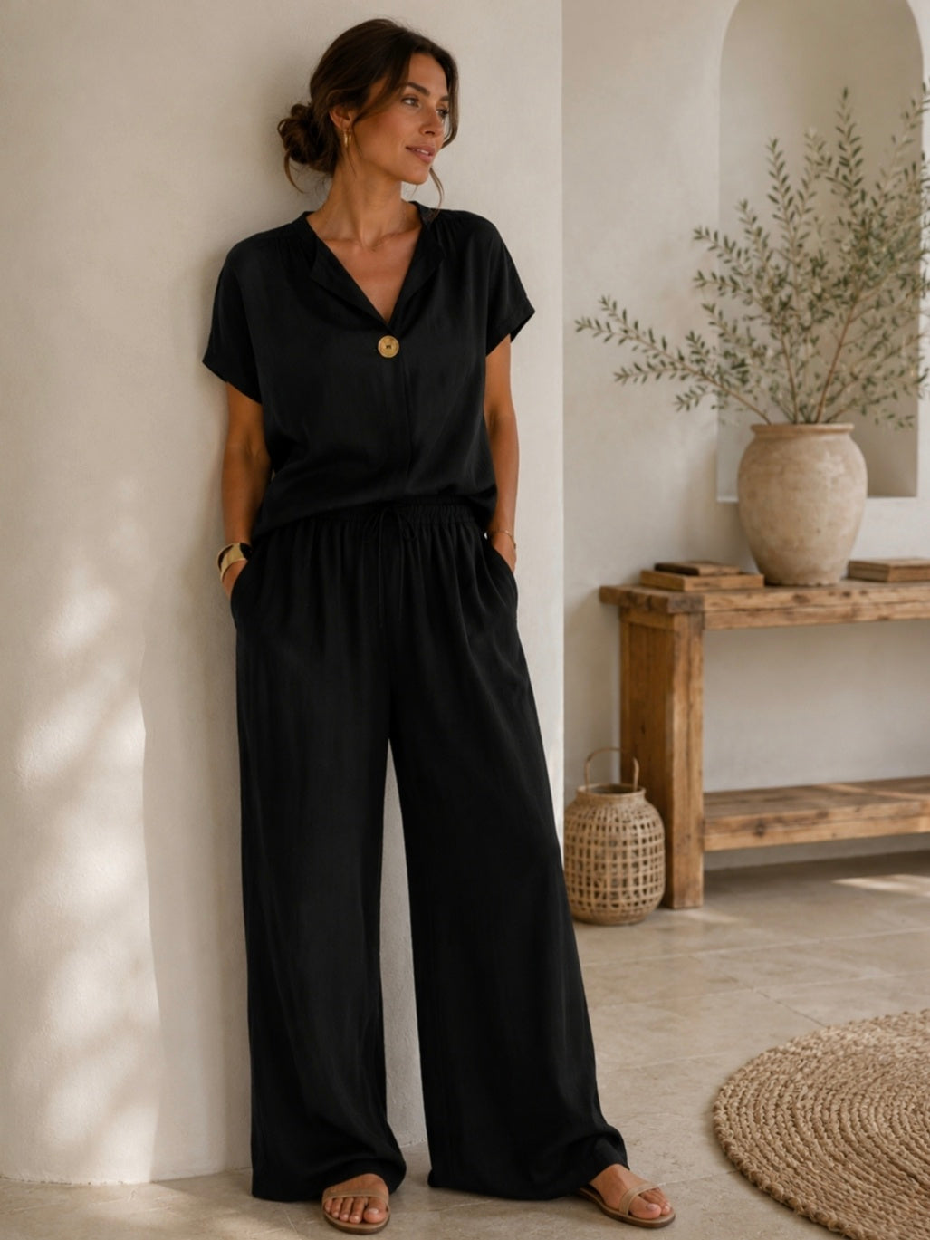 Woman wearing a black outfit standing in a room with a wooden table and plants.
