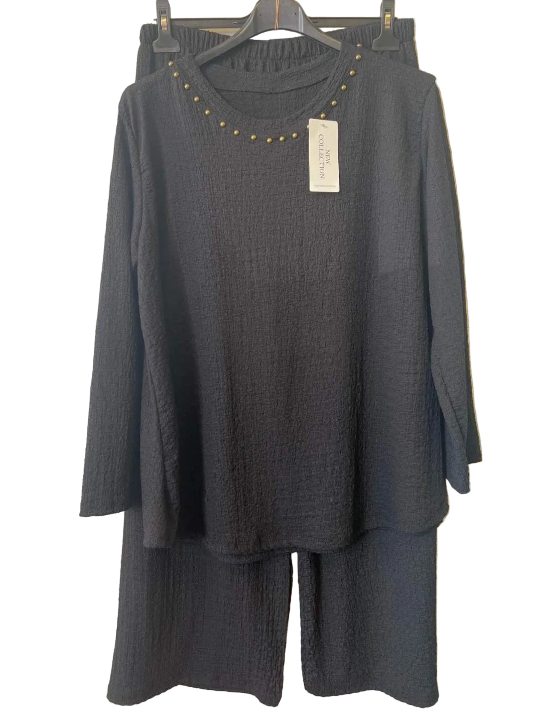 A black textured two-piece set consisting of a long-sleeve top with gold stud detailing around the neckline and matching wide-leg pants