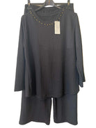 A black textured two-piece set consisting of a long-sleeve top with gold stud detailing around the neckline and matching wide-leg pants
