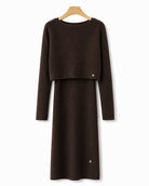A dark brown ribbed knit long-sleeve dress with a cropped long-sleeve top overlay, hanging on a wooden hanger against a plain white background.