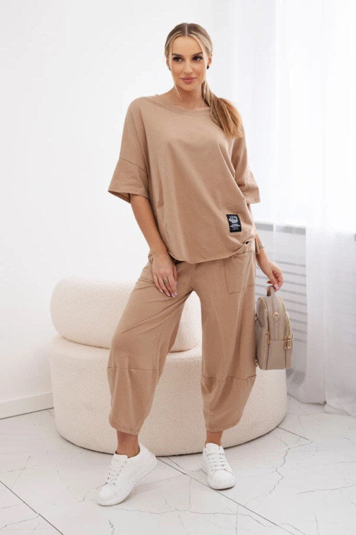 Woman in beige outfit standing next to a white chair with a white background