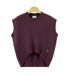 A sleeveless crewneck knit sweater vest in deep plum purple, hanging on a wooden hanger against a plain white background. The vest features a curved hemline with ribbed detailing and a small silver heart charm on the lower right side.
