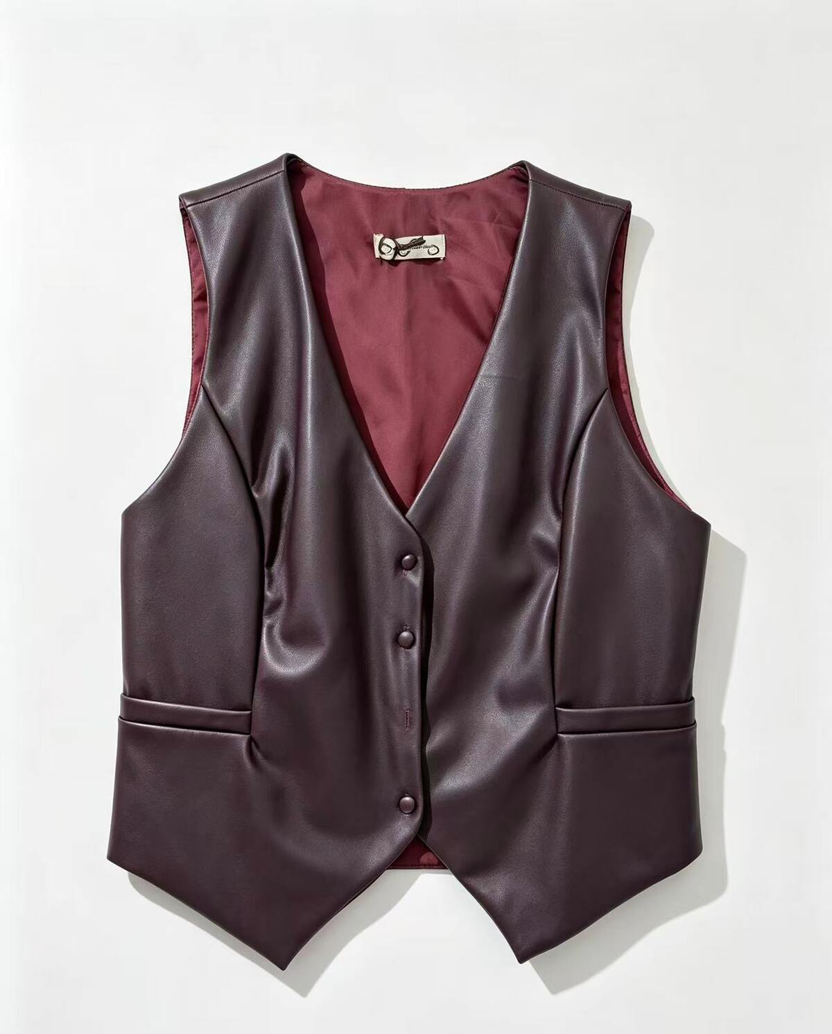 A dark plum faux-leather vest with a V-neck, three-button front, and side pockets, displayed flat against a light off-white background.