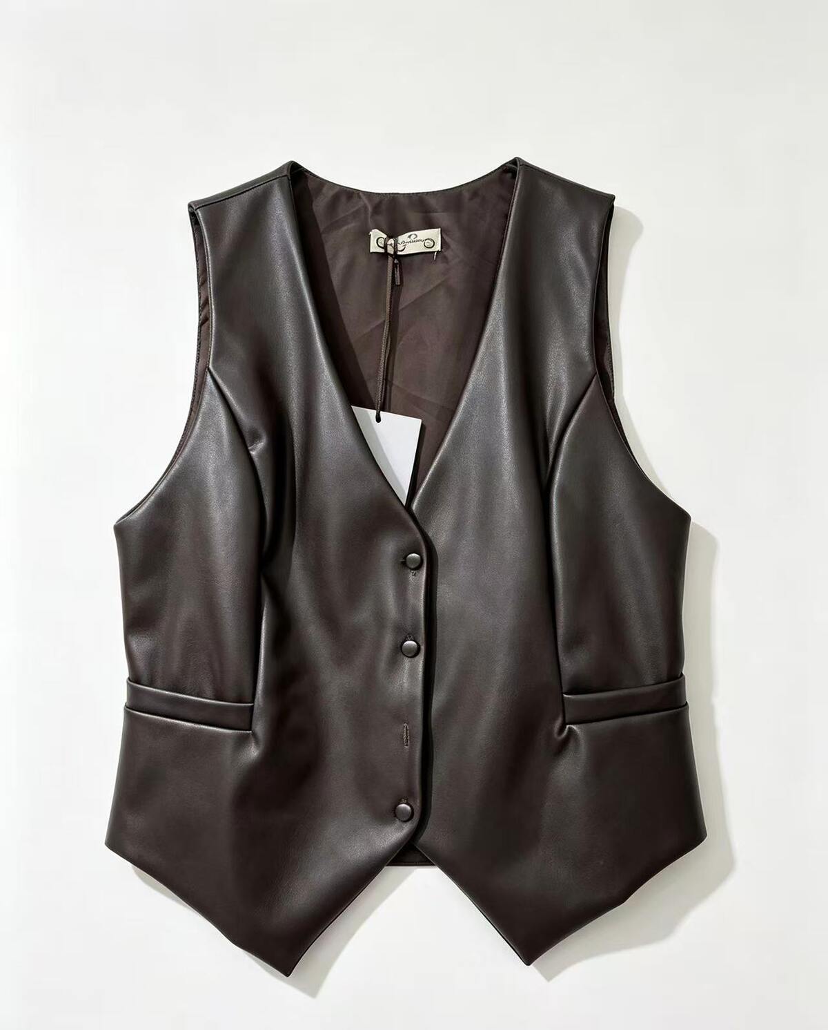 A dark brown faux-leather vest with a V-neck, button-front closure, and side pockets, laid flat against a light off-white background.