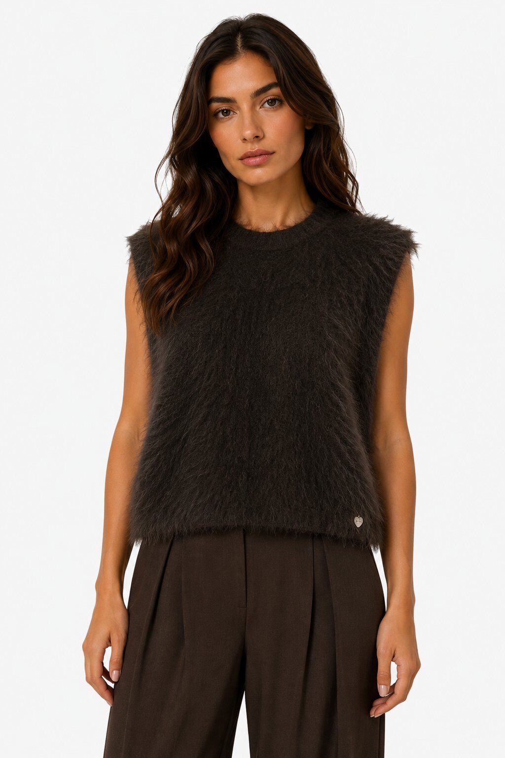 A woman modeling a sleeveless, dark brown fuzzy knit vest with a small gold button detail on the lower right, paired with dark brown wide-leg trousers, against a plain white background.