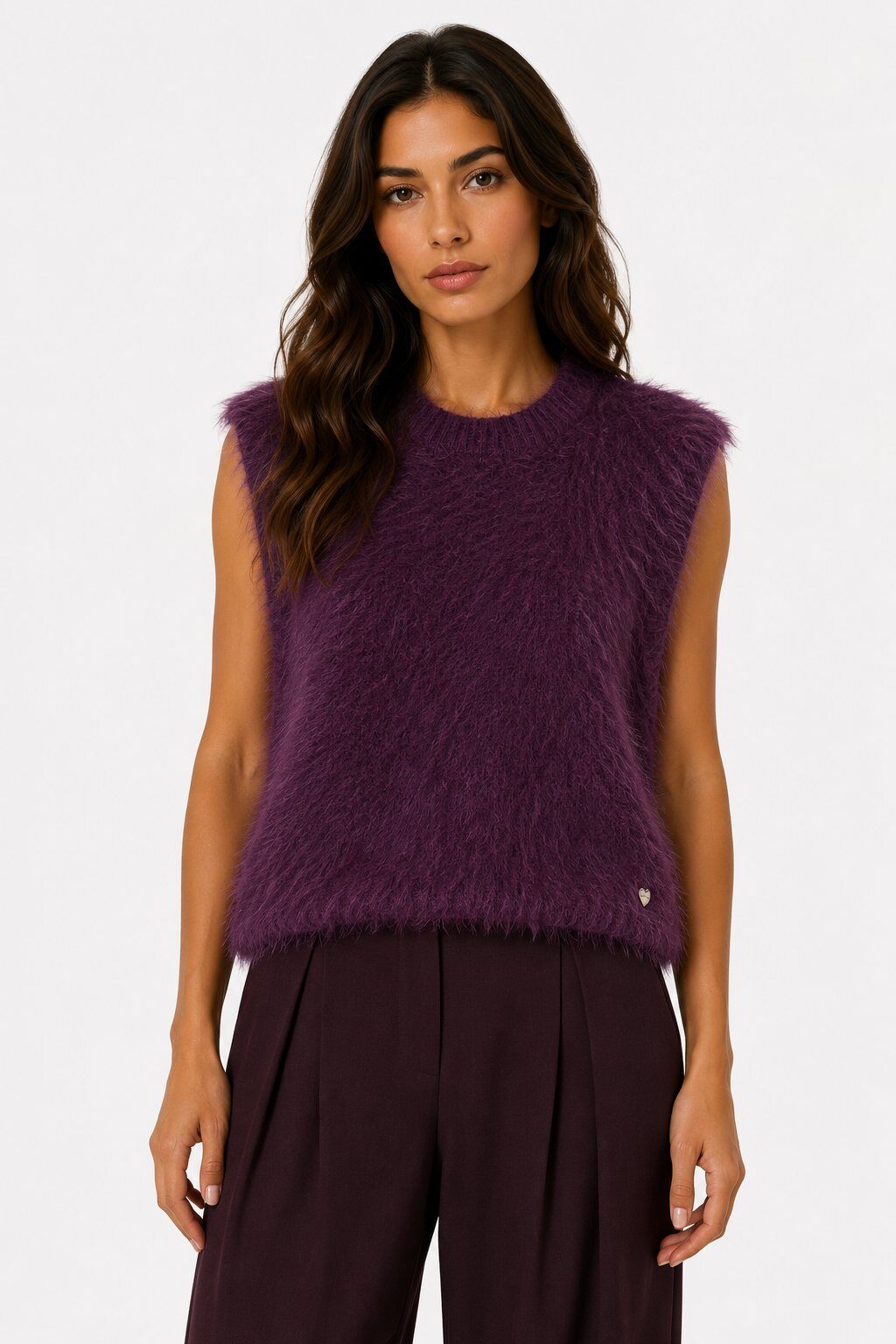A woman modeling a sleeveless, fuzzy knit top in a deep plum purple color, paired with dark pleated trousers, against a plain white studio background.