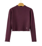 A dark plum purple ribbed knit long-sleeve crop top sweater hanging on a wooden hanger against a plain white background. The bottom hem has a scalloped edge, and there is a tiny silver heart detail on the lower left side.