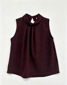 A sleeveless dark burgundy top with a high gathered mock neck and front pleats, laid flat against a light off-white background.