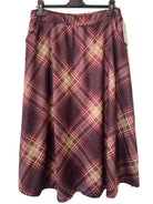 A pleated A-line skirt in a burgundy and beige plaid pattern, hanging on a black hanger against a textured gray wall.