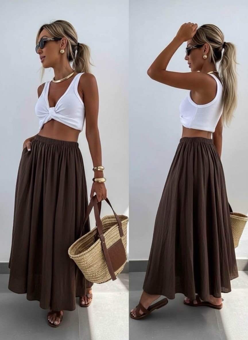 Woman wearing a white top and brown skirt with a straw bag indoors.