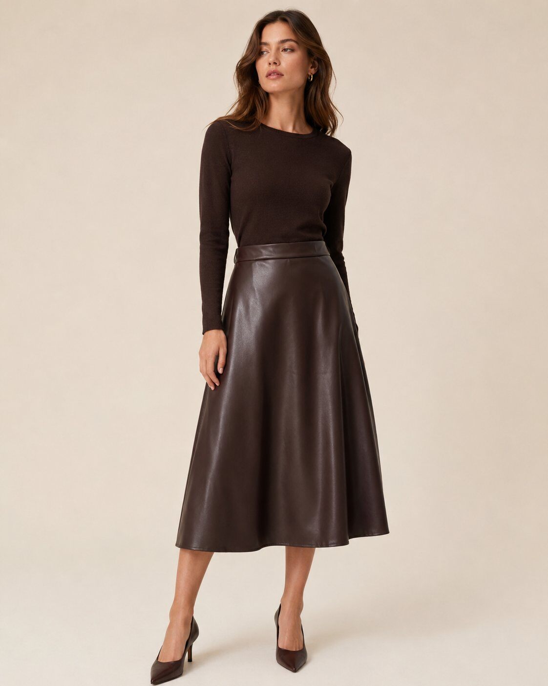 A woman modeling a dark brown long-sleeve knit top and a matching dark brown leather midi skirt 