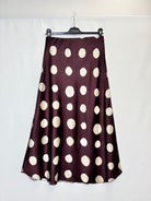 A dark plum purple satin skirt with large cream polka dots, hanging on a black hanger against a white fabric backdrop.
