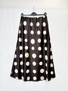 A black satin midi skirt with large cream polka dots, hanging on a black hanger against a white background.