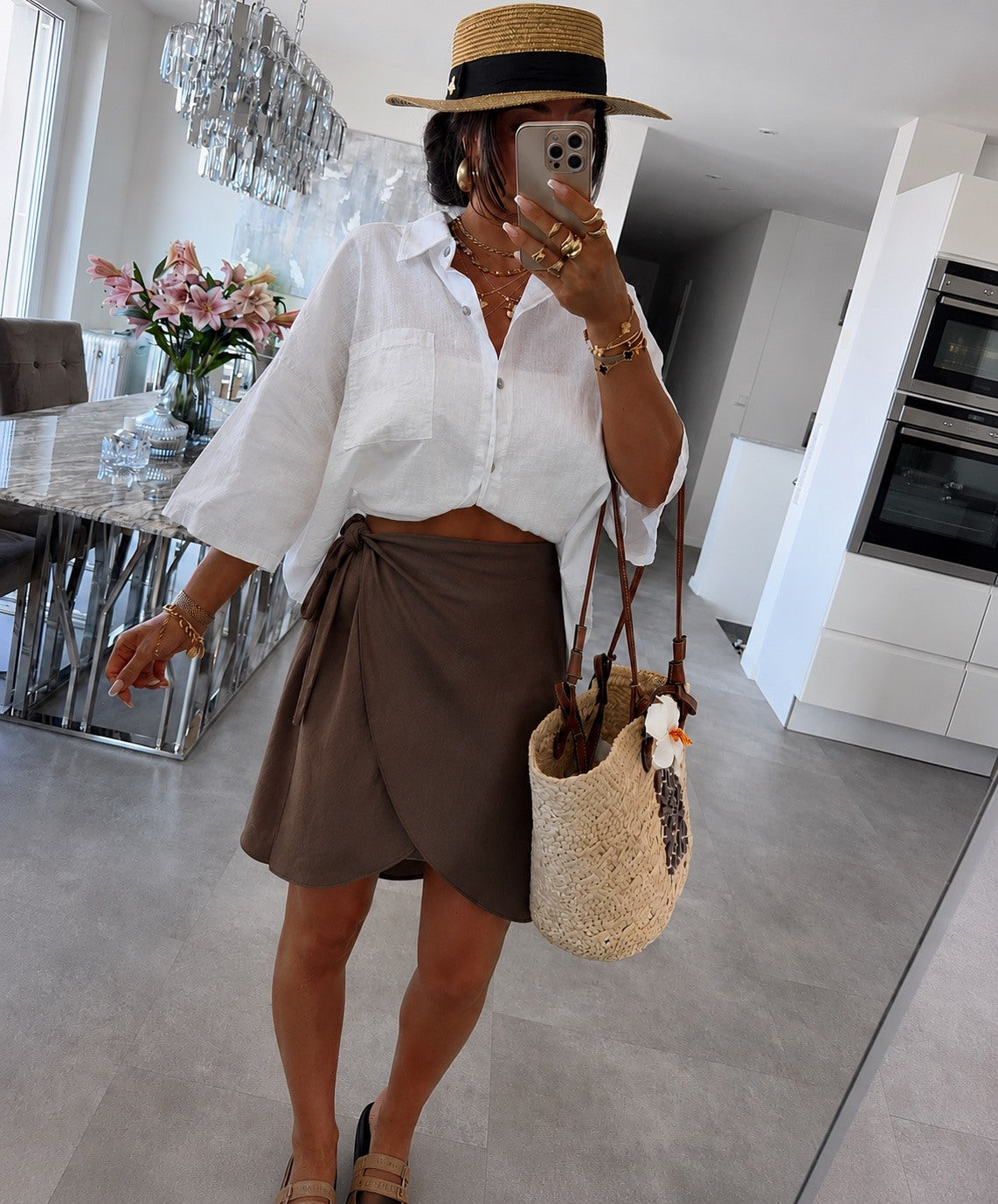 A woman wearing a white cropped button-up shirt, a brown wrap-style mini skirt