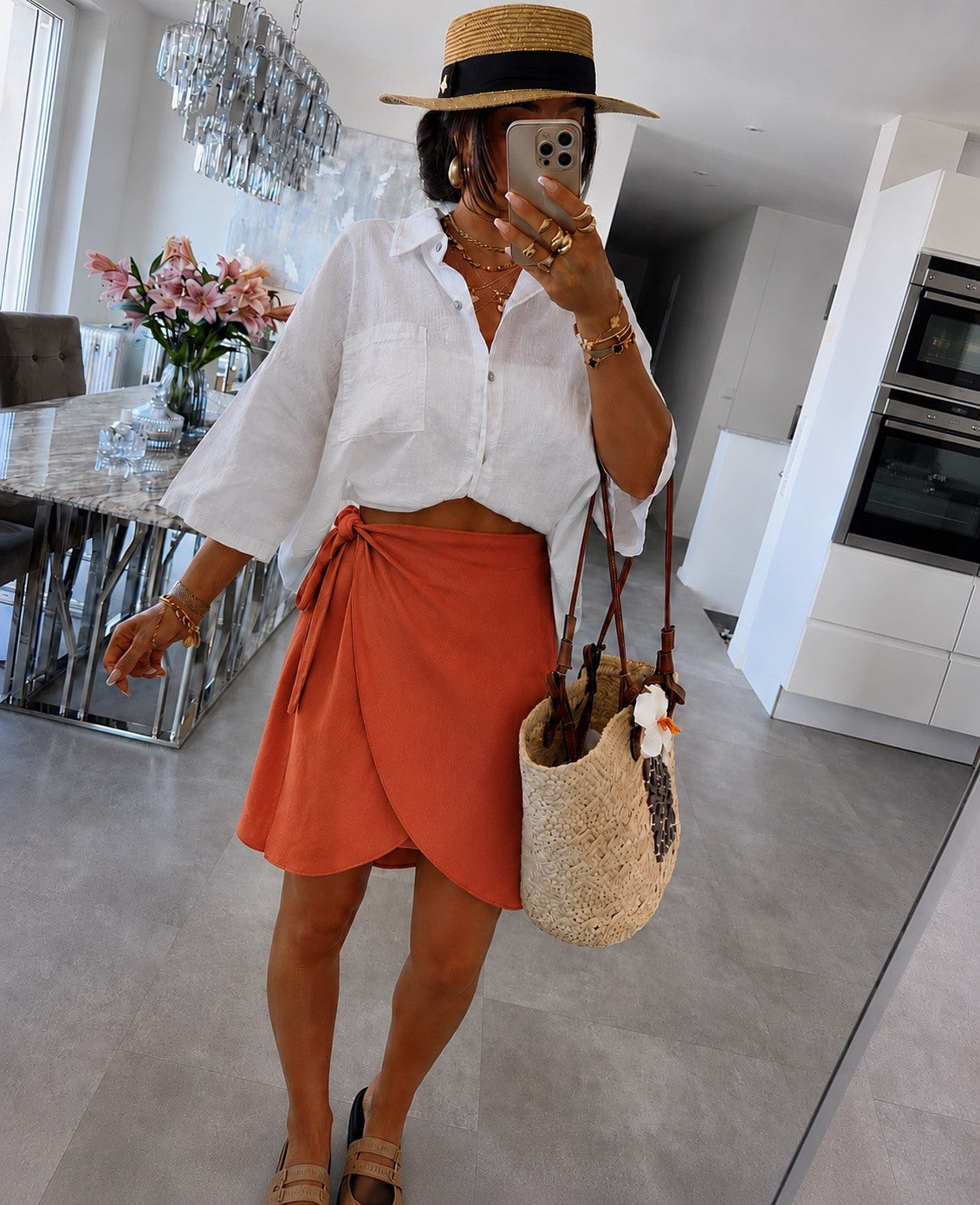 A woman wearing a white button-down shirt, a rust-orange wrap skirt
