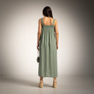 A woman viewed from behind wearing a green sleeveless maxi dress with a smocked bodice and straps