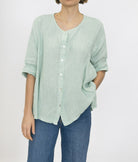 Person wearing a light green button-up shirt and blue jeans on a white background