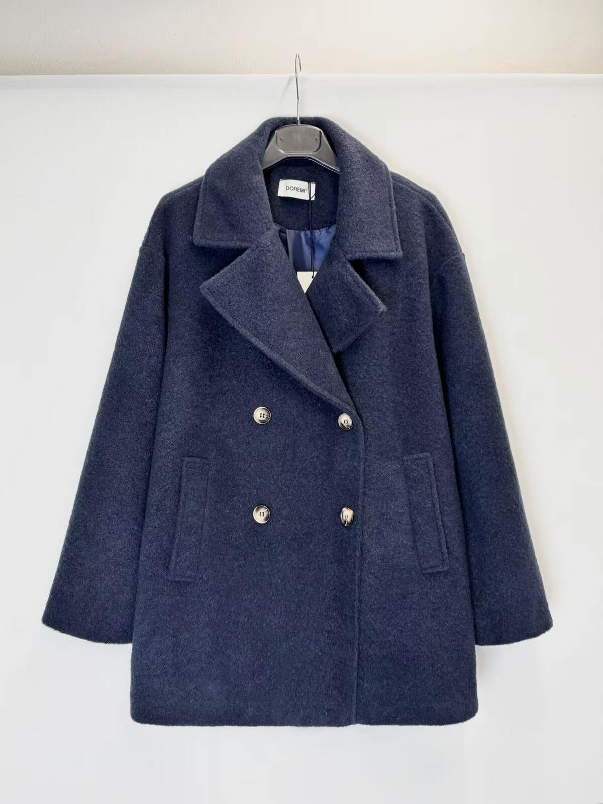 A navy blue double-breasted coat with silver buttons, hanging on a black hanger against a plain white wall.