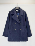 A navy blue double-breasted coat with silver buttons, hanging on a black hanger against a plain white wall.