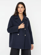A woman modeling a navy blue double-breasted coat with silver buttons, photographed against a clean white studio background.