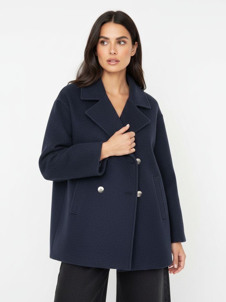 A woman modeling a navy blue double-breasted coat with silver buttons, photographed against a clean white studio background.