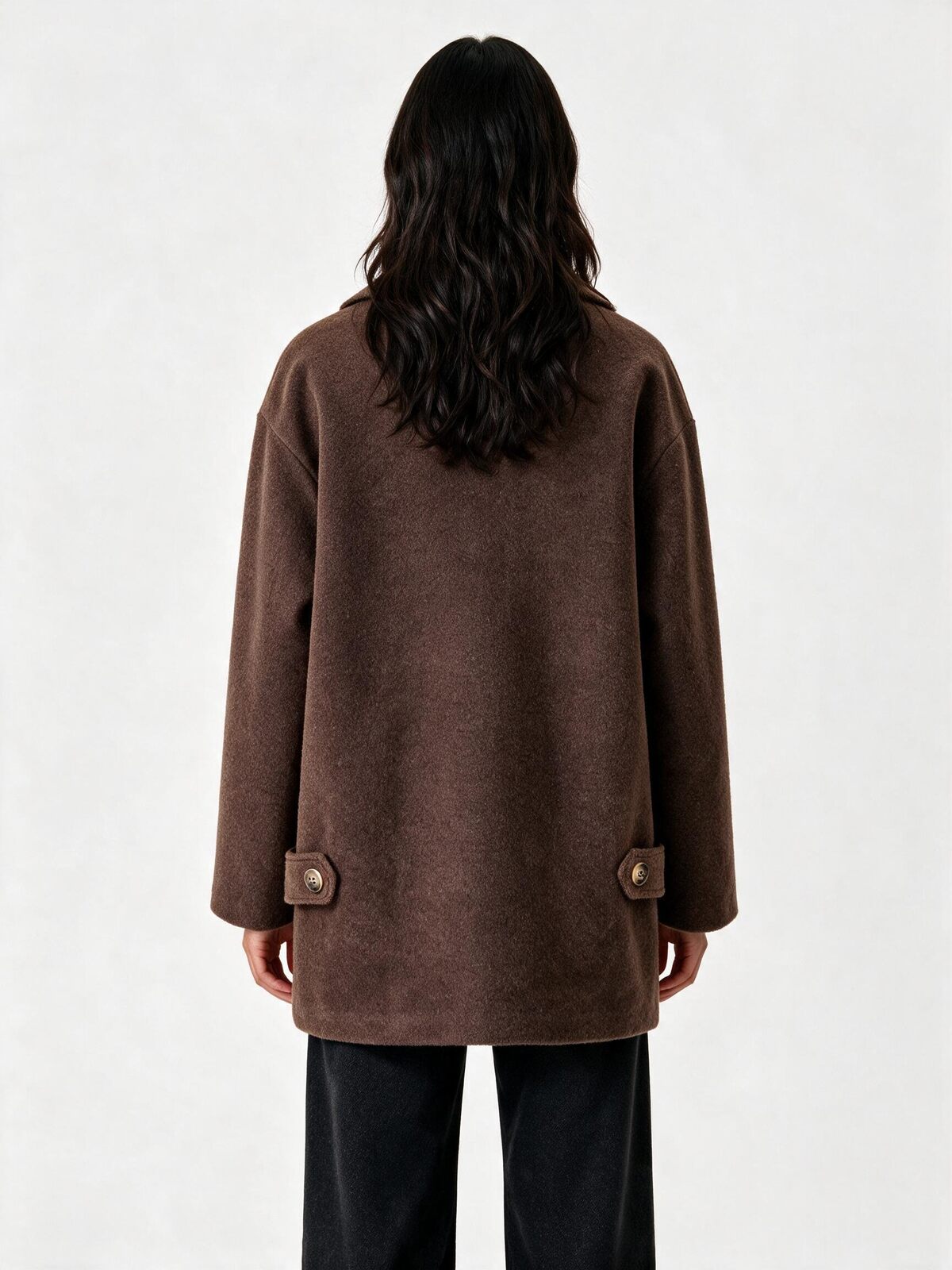 A model viewed from the back wearing a brown textured coat with button details on the back cuffs and black wide-leg pants, set against a plain light gray background.