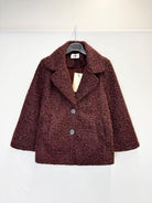 A textured, boucle-style dark burgundy coat with wide lapels and two front buttons, hanging on a black hanger against a plain white wall.