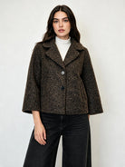 A woman modeling a cropped, dark brown textured tweed jacket with wide three-quarter sleeves, worn over a white turtleneck and black wide-leg jeans, against a plain light gray background.
