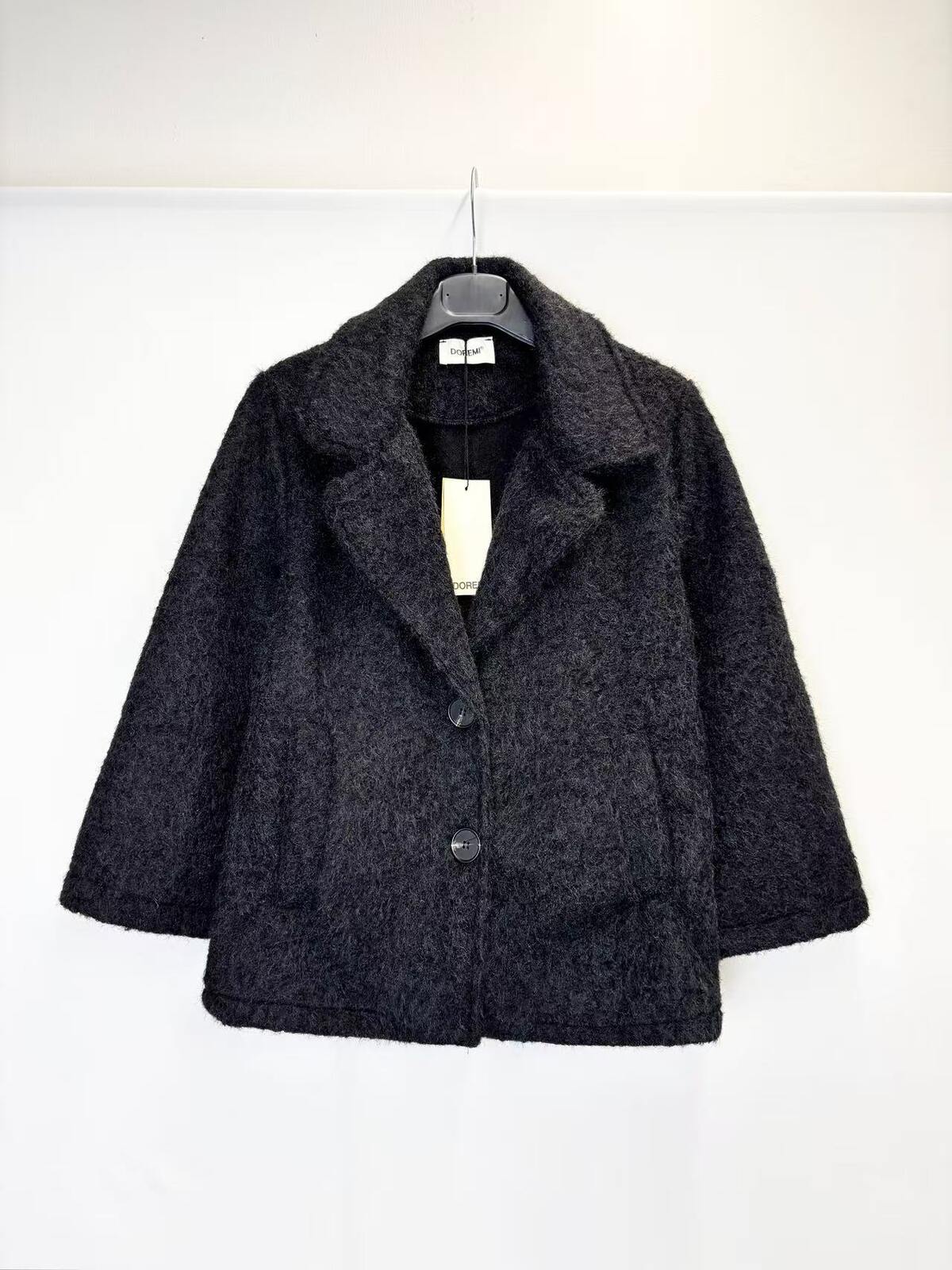 A dark charcoal gray textured wool-blend jacket with a wide collar and three front buttons, hanging on a black hanger against a plain white wall.