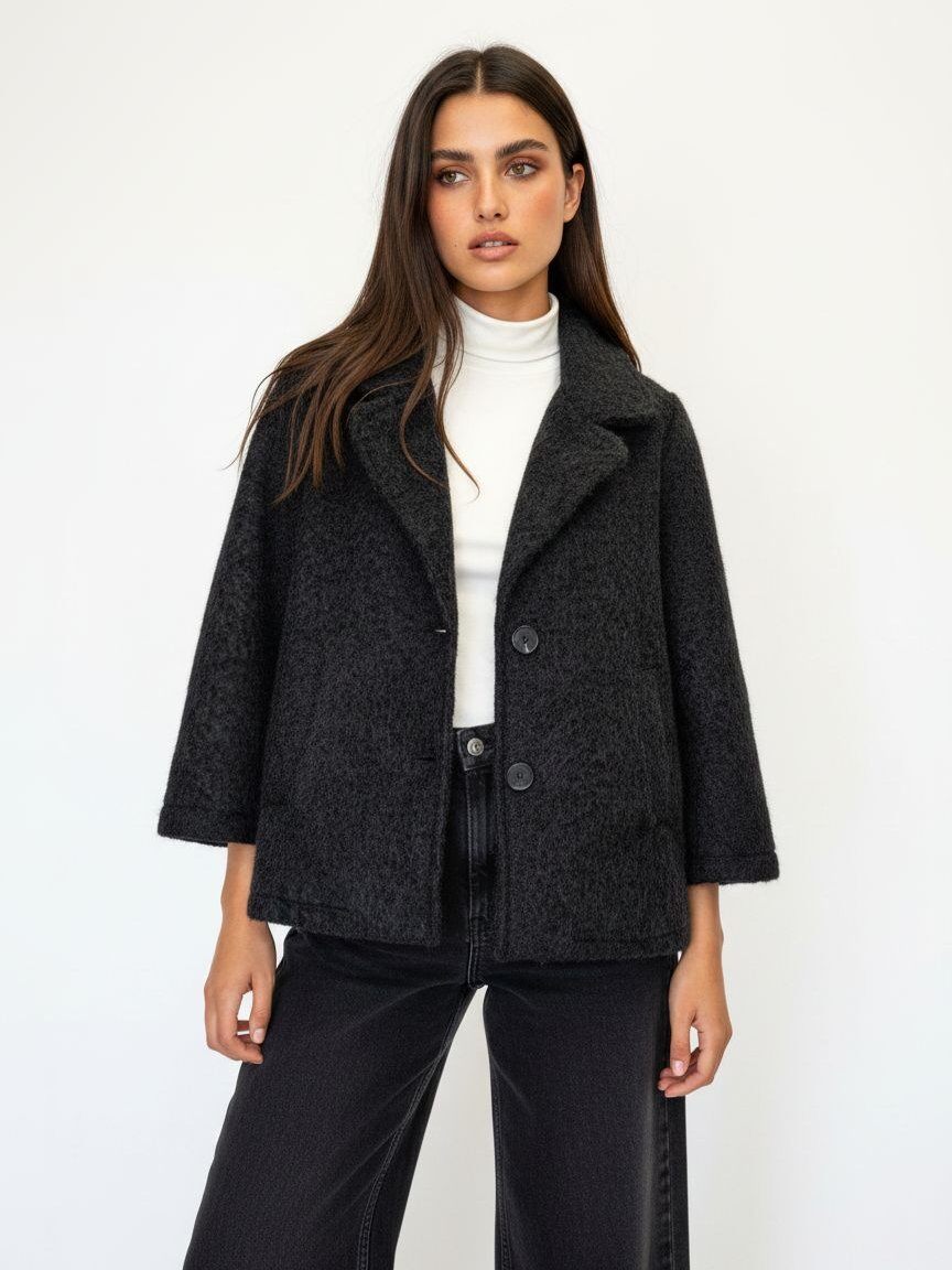 A woman modeling a dark charcoal gray textured wool-blend coat with a white turtleneck and black wide-leg jeans against a plain white studio background.