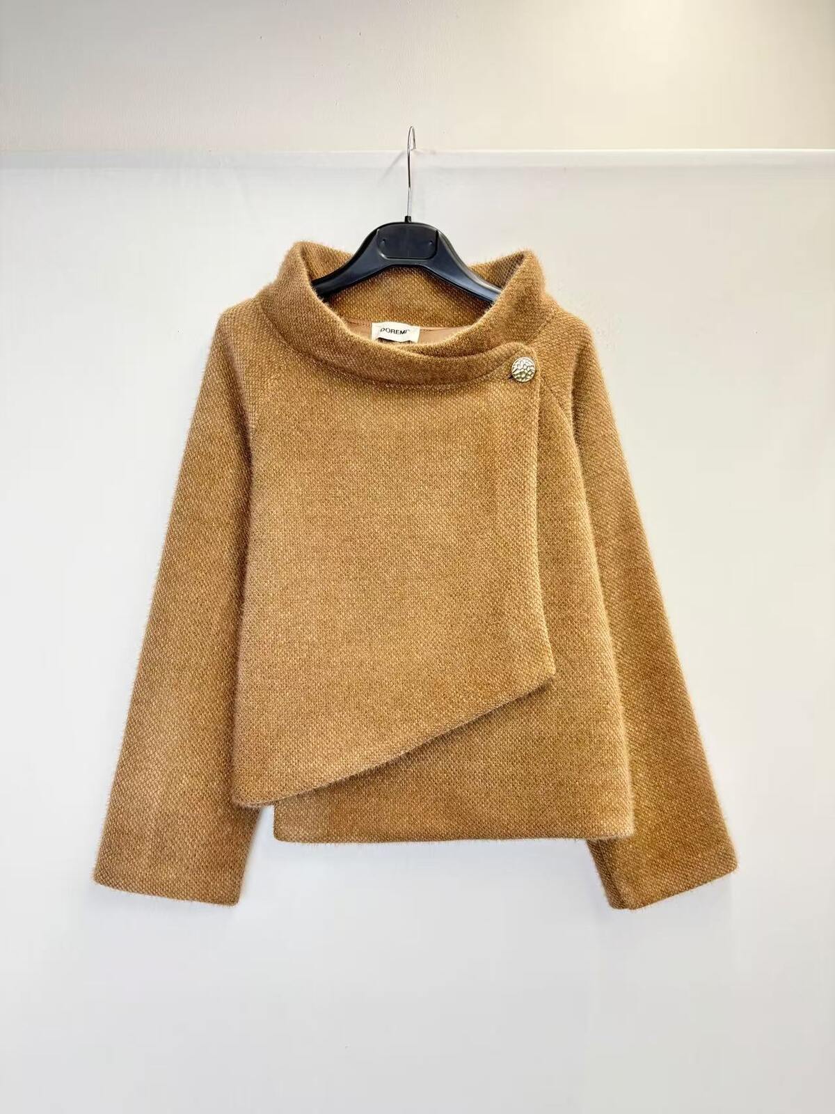 A camel brown fuzzy asymmetrical wrap sweater hanging on a black hanger against a plain white wall.