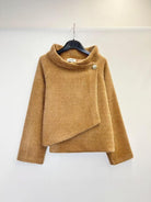 A camel brown fuzzy asymmetrical wrap sweater hanging on a black hanger against a plain white wall.